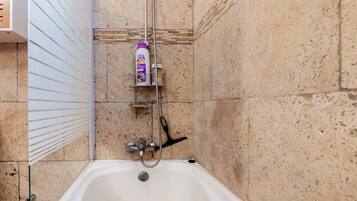 Une salle de bain équipée d’une baignoire, d’une douche et d’une étagère où sont rangés les articles de toilette.
