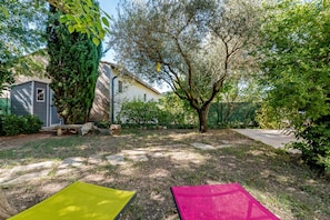 Un jardin à l’arrière d’une maison, avec un chemin en pierre, un petit abri de jardin et un arbre.