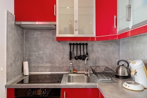 Une cuisine avec des meubles de rangement rouges, un évier en acier inoxydable, une plaque de cuisson à induction et une bouilloire.