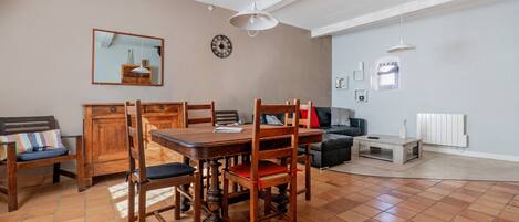 A dining area with a wooden table and chairs, a mirror, a clock, and a sofa in a living room with a tiled floor.