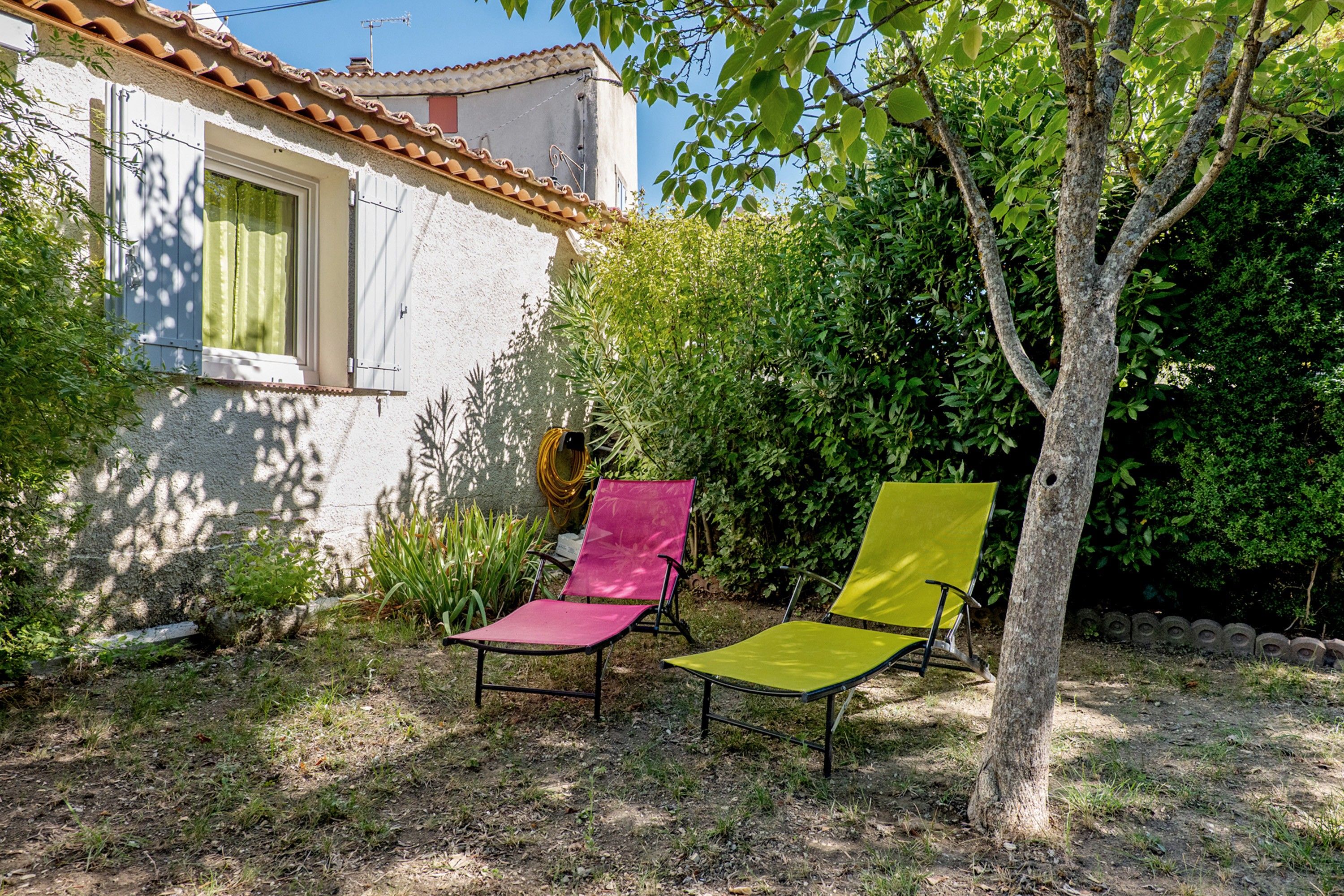 A garden with two chairs, a tree, and a building with a tiled roof.