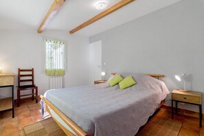 A bedroom with a bed, a chair, a desk, and a window with curtains.