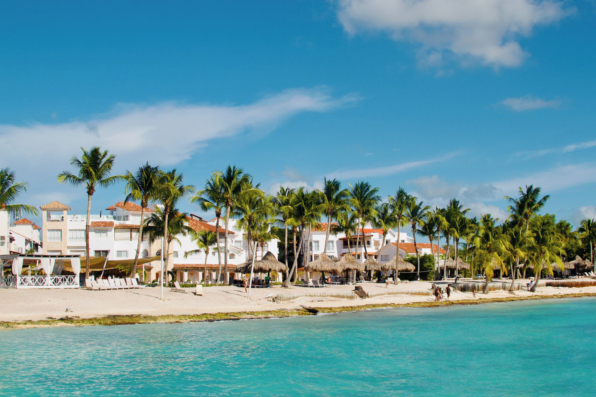 A beachfront hotel with multiple buildings, palm trees, and a clear blue sky.