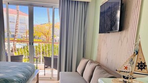 Hotellihuone, jossa on sänky, sohva, televisio ja pieni keittonurkkaus.