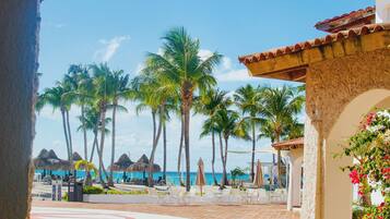 A paved patio area with palm trees, a beach view, and a building with a tiled roof.