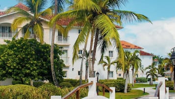 A paved pathway leading to a white building with a red-tiled roof, surrounded by palm trees and greenery.