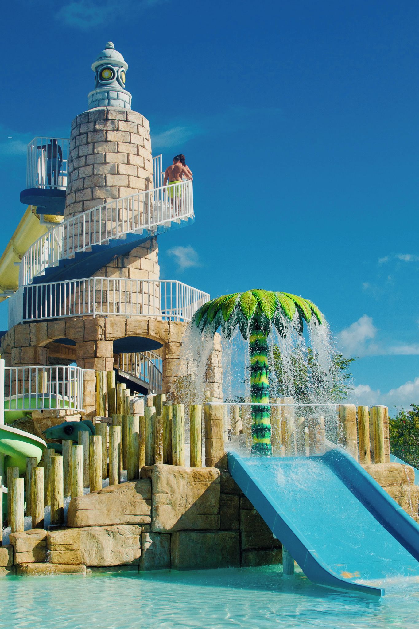 A water park with a large water slide, a water fountain, and a stone structure with a viewing platform.