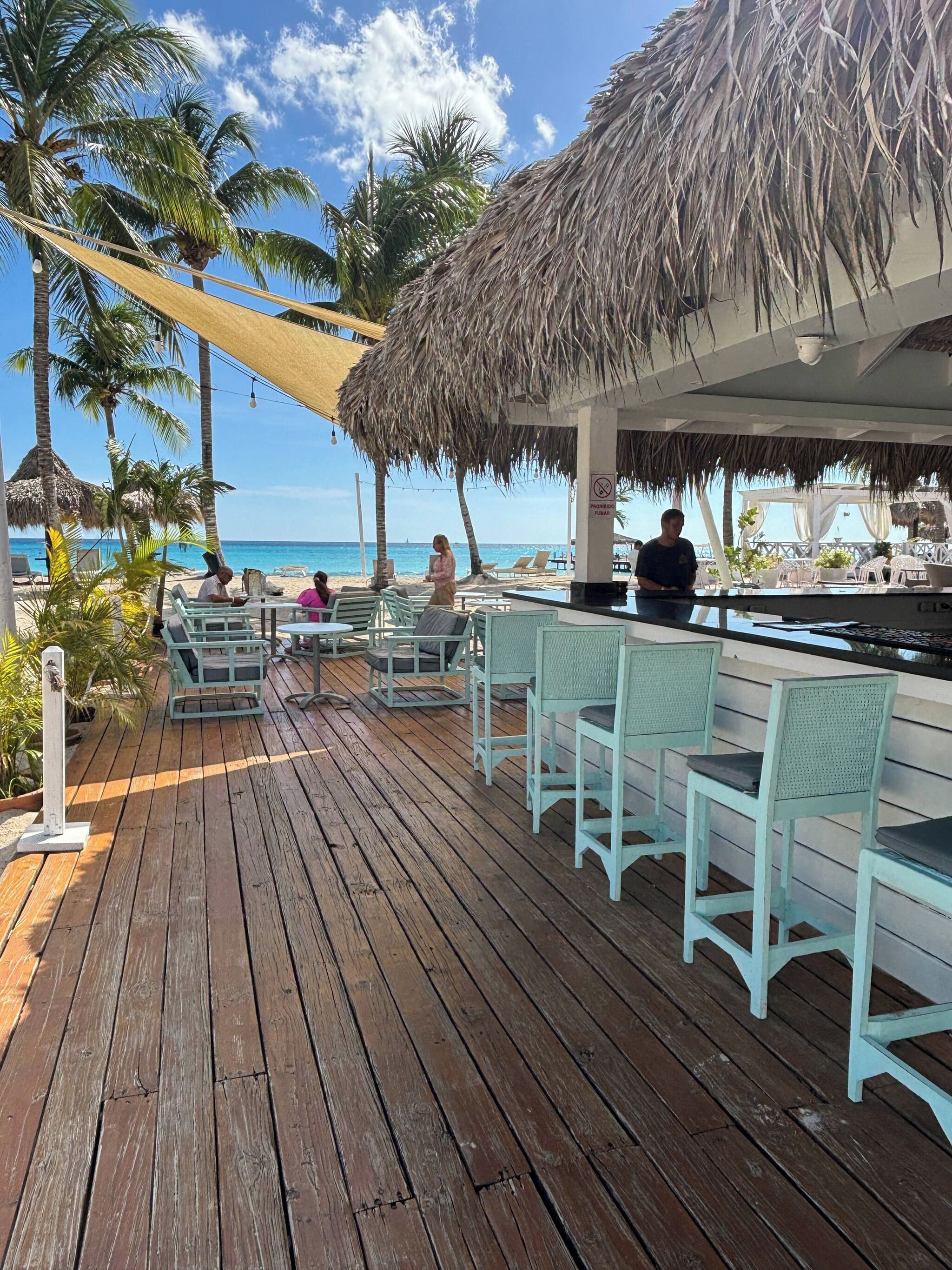 A wooden deck with outdoor seating, a bar area, and a view of the beach and ocean.