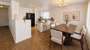 Eine moderne Küche mit weißen Schränken, einem schwarzen Kühlschrank und einem Essbereich mit einem Holztisch und Stühlen.