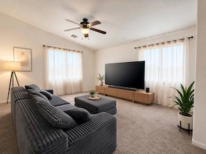 Een moderne woonkamer met een hoekbank, een flatscreen televisie, een plafondventilator en een potplant.