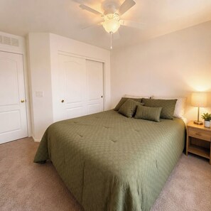 A bedroom with a bed, a nightstand, a lamp, and a ceiling fan.