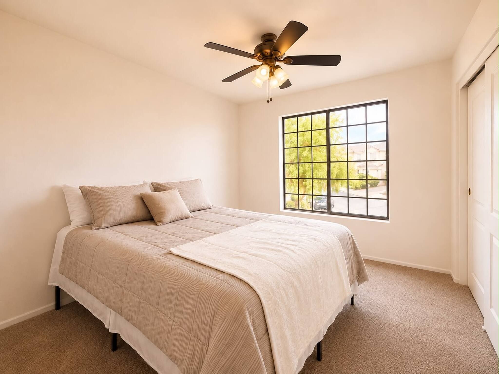 Une chambre à coucher avec un lit, un ventilateur de plafond, une fenêtre donnant sur un beau paysage et un sol recouvert de moquette.