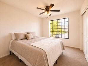 Una camera da letto con un letto, una ventola a soffitto, una finestra vista e pavimento tappezzato.