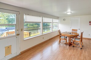 Une pièce comprenant une table à manger et des chaises, de grandes fenêtres, une porte et un luminaire au plafond.