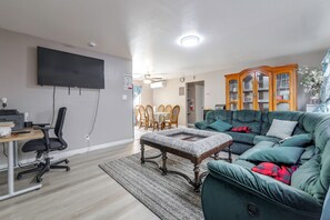 A living room with a green sofa, a coffee table, a TV, and a dining area with chairs and a table.