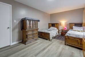 Quarto com duas camas de madeira, cômoda e mesa de cabeceira com abajur.