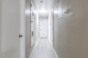 A hallway with white walls and doors, leading to a room with a white door.