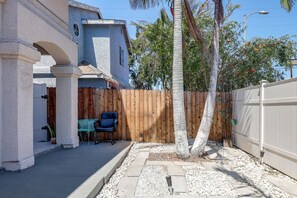 A residential backyard with a wooden fence, a palm tree, and a blue chair.