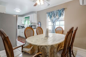 A dining area with a round table covered in a floral tablecloth, surrounded by wooden chairs.