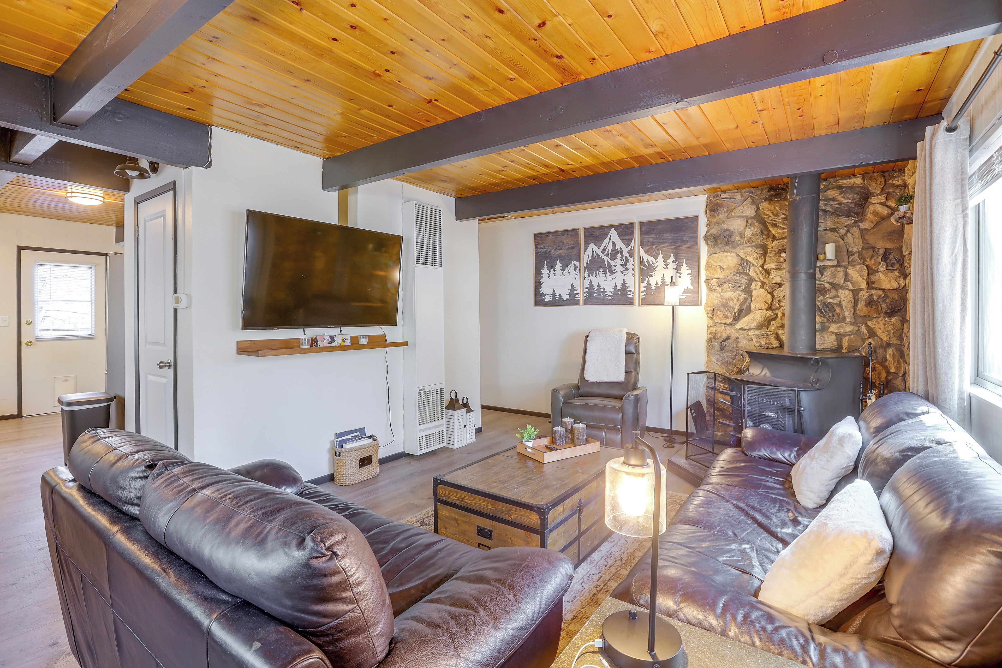 A living room with leather sofas, a flat-screen TV, a stone wall, and a fireplace.