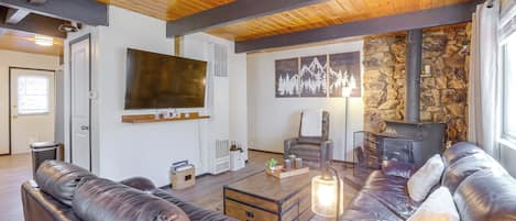 A living room with leather sofas, a flat-screen TV, a stone wall, and a fireplace.