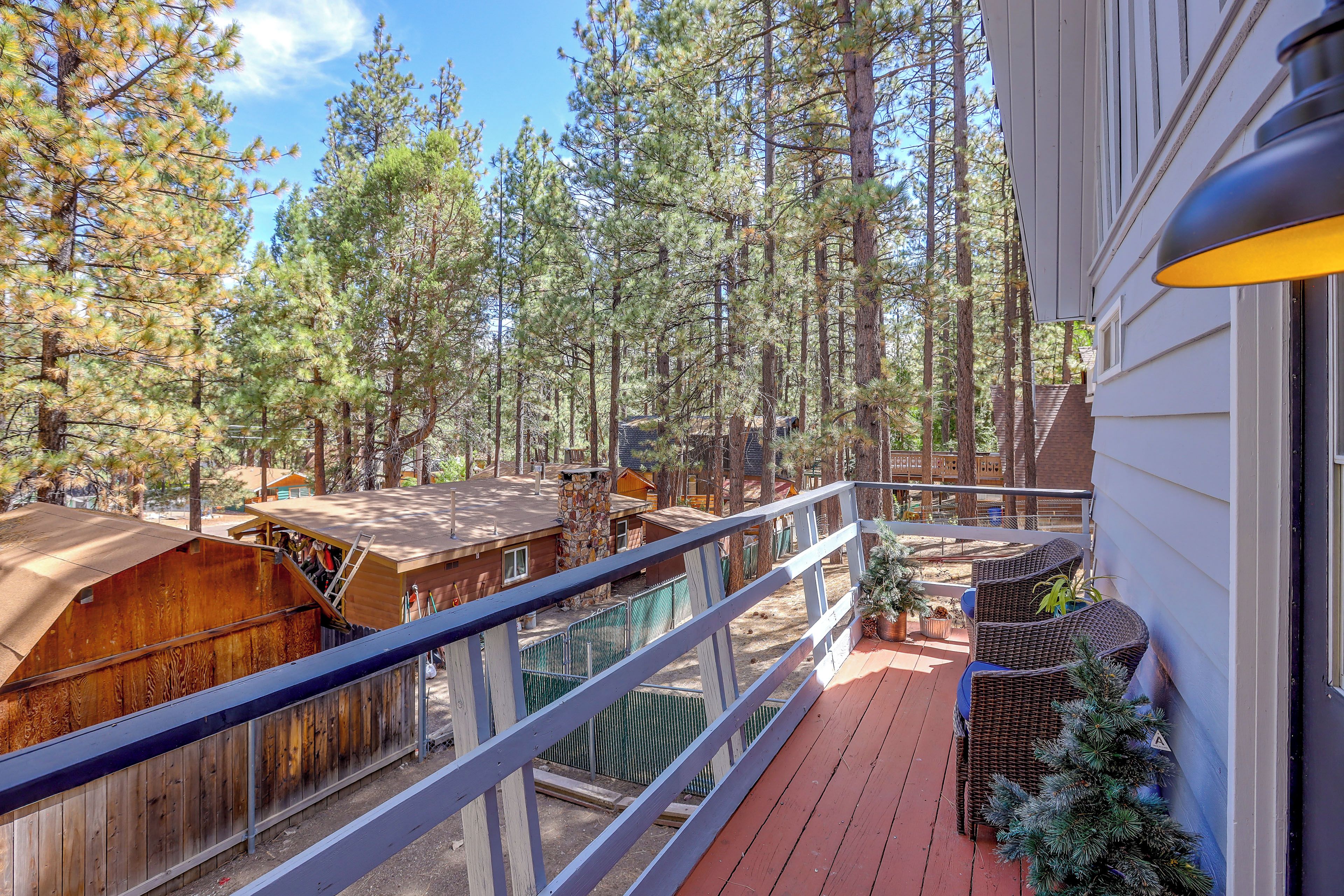 A balcony with a view of a forested area, wooden structures, and a stone chimney.