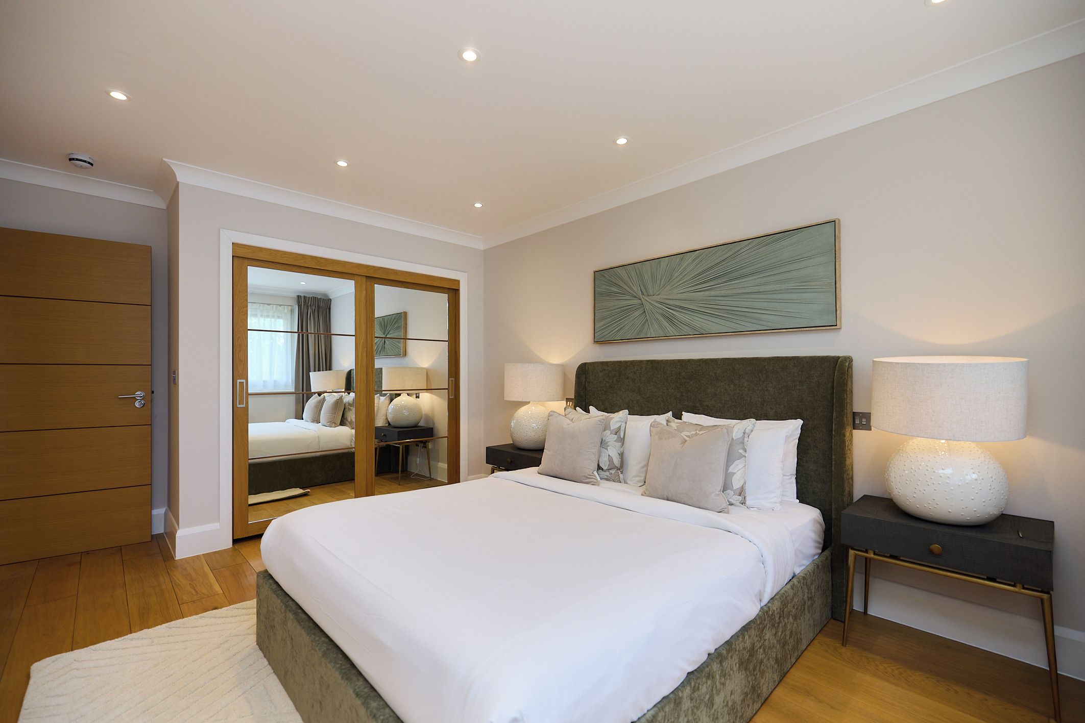 A bedroom with a bed, bedside tables, a mirror, and a ceiling light.