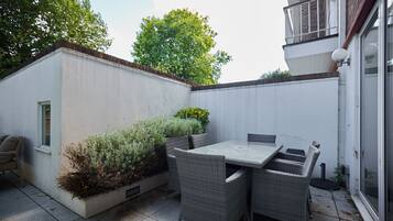 Un patio con mesa y sillas, una ventana pequeña y una pared blanca.