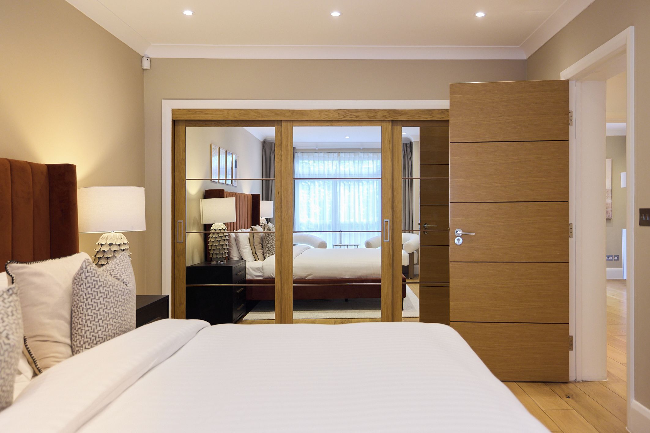 A hotel room with a large bed, a wardrobe, a bedside table with lamps, and a view through a sliding door to a balcony.