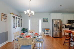 A modern kitchen with white cabinets, a stainless steel refrigerator, and a dining area with a glass table and wicker chairs. - Lake Marion Retreat | Dock Days & Backyard Nights (Summerton)