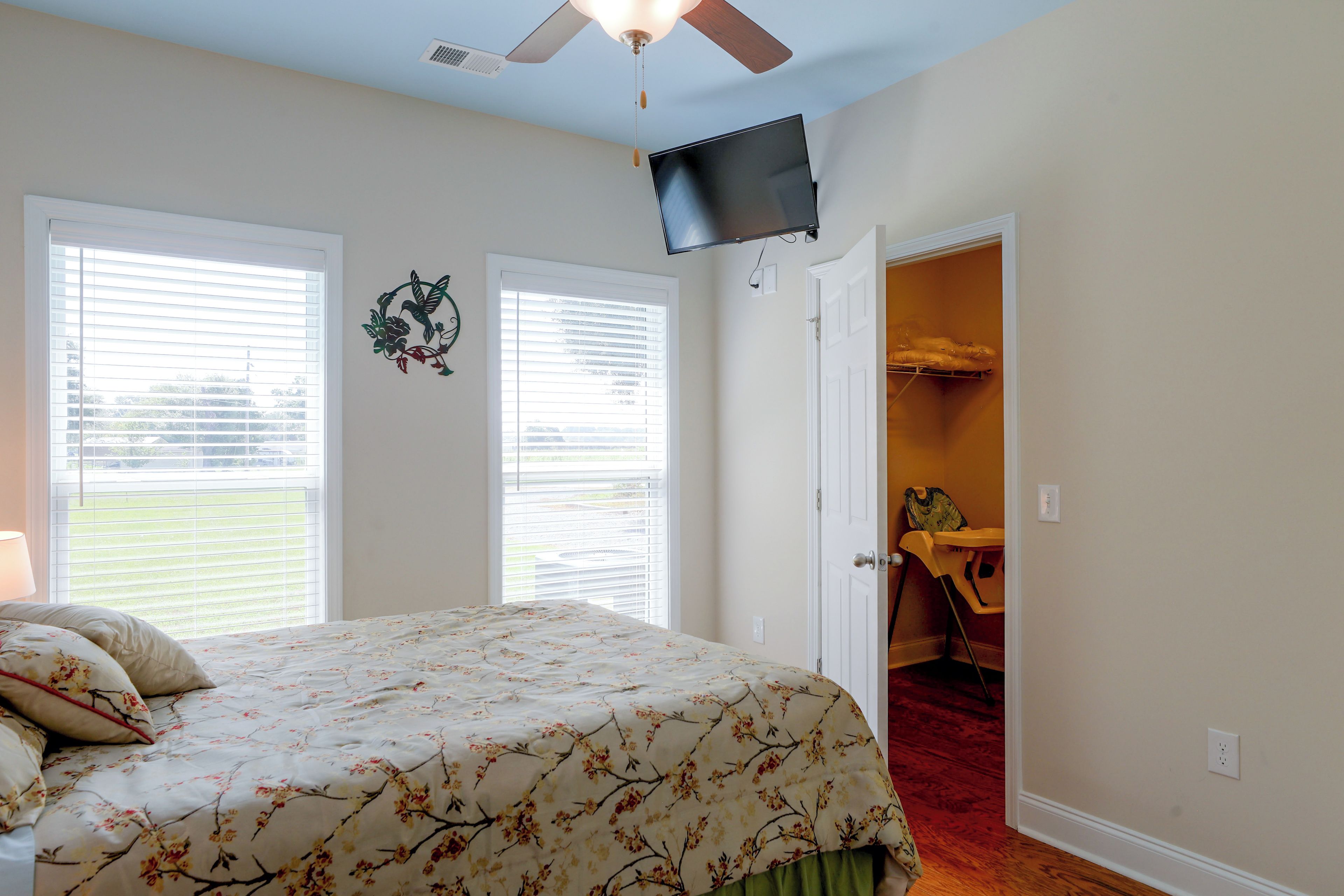 A bedroom with a bed, a ceiling fan, a TV mounted on the wall, and a door leading to a closet.