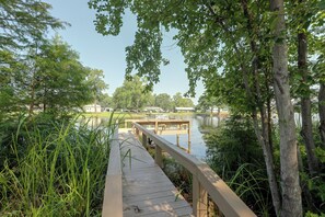 A wooden boardwalk leading to a dock over a calm body of water, surrounded by lush greenery and trees. - Lake Marion Retreat | Dock Days & Backyard Nights (Summerton)
