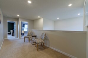 A hallway with carpeted flooring, two upholstered chairs, a small round table, and recessed ceiling lighting. - Solterra Resort Home w/ AI Vending & Private Pool! (Davenport)