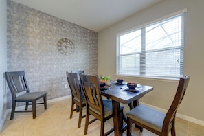 A dining area with a table set for four, chairs, a clock on the wall, and a window with blinds. - Solterra Resort Home w/ AI Vending & Private Pool! (Davenport)
