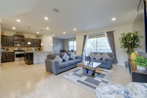 A modern living room with a grey sofa, a coffee table, and a kitchen area with dark cabinets and a microwave. - Solterra Resort Home w/ AI Vending & Private Pool! (Davenport)