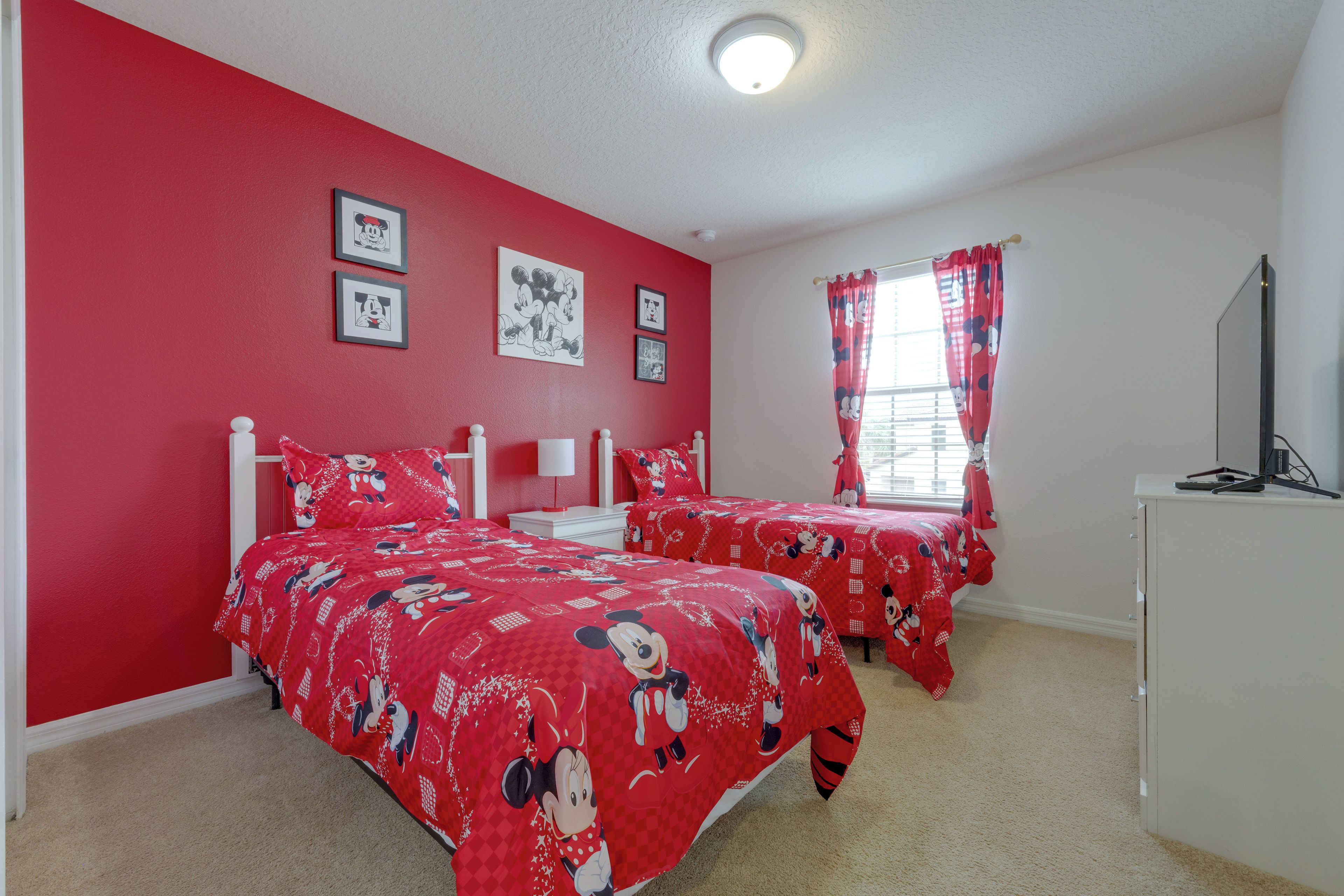 A room with two beds, red walls, and Mickey Mouse themed bedding.
