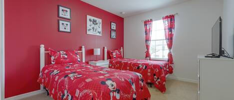 Une chambre avec deux lits, des murs rouges et de la literie aux motifs de Mickey Mouse.