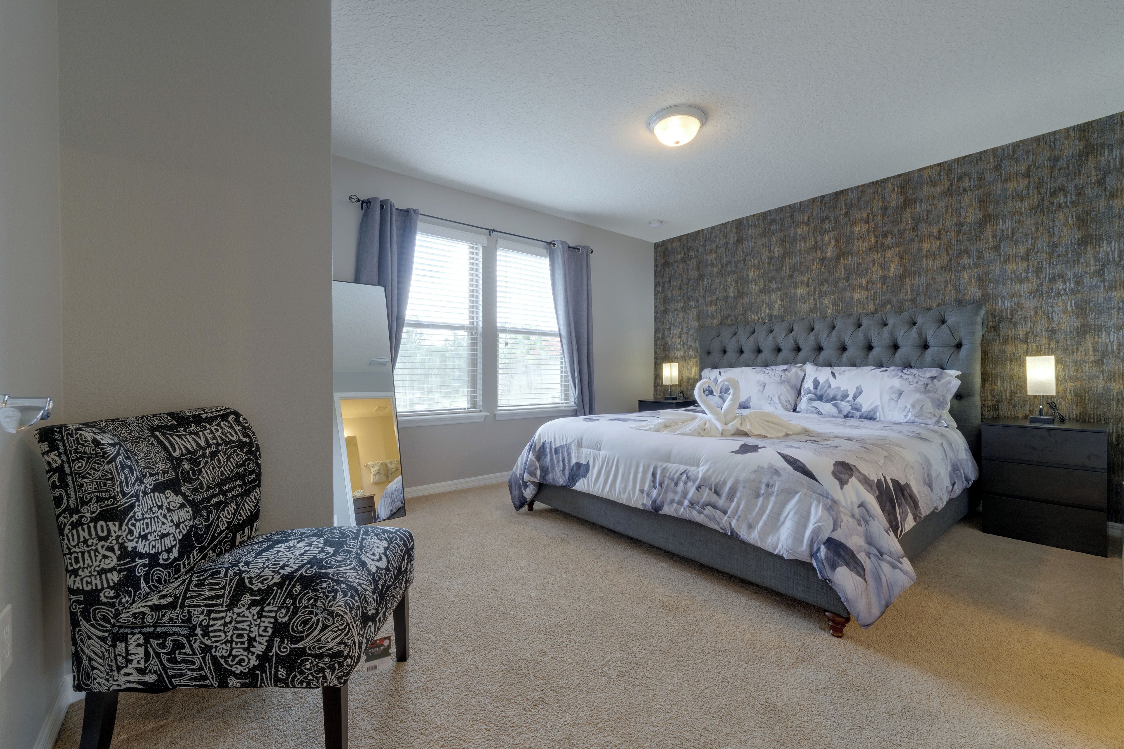 A bedroom with a large bed, a chair, a nightstand, and a window with curtains.