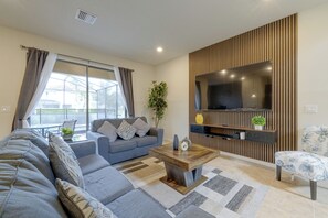 A modern living room with a sofa, coffee table, and a flat-screen TV mounted on a wooden panel wall. - Solterra Resort Home w/ AI Vending & Private Pool! (Davenport)