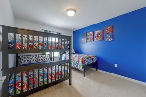 Une chambre avec des lits superposés et un mur bleu, décorée avec du linge de lit et des œuvres murales sur le thème des super-héros.