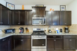 A kitchen with dark wooden cabinets, a stainless steel microwave, a coffee maker, and a stove. - Solterra Resort Home w/ AI Vending & Private Pool! (Davenport)