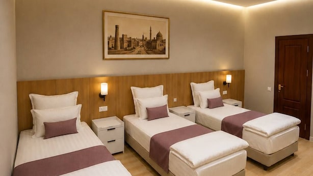 A hotel room with three beds, wooden headboards, a cityscape painting, and a wooden floor. - Darvaza Boutique Hotel (Bukhara)