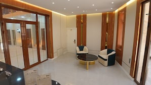 A modern hotel lobby with a reception desk, two armchairs, a small round table, and a glass door entrance. - Darvaza Boutique Hotel (Bukhara)
