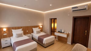 A hotel room with two beds, a desk, a chair, an air conditioning unit, and a door. - Darvaza Boutique Hotel (Bukhara)