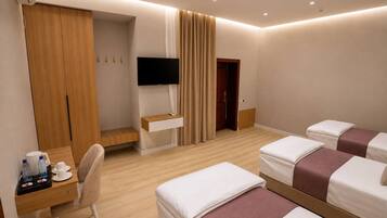 Habitación de hotel con escritorio, dos camas, televisor y armario.