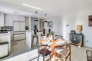 Cozinha moderna com armários brancos, área de refeições com mesa e cadeiras de madeira, e uma ilha de cozinha.