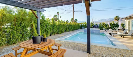 Una mesa de picnic de madera con bancos, una piscina y un área techada con una pérgola.