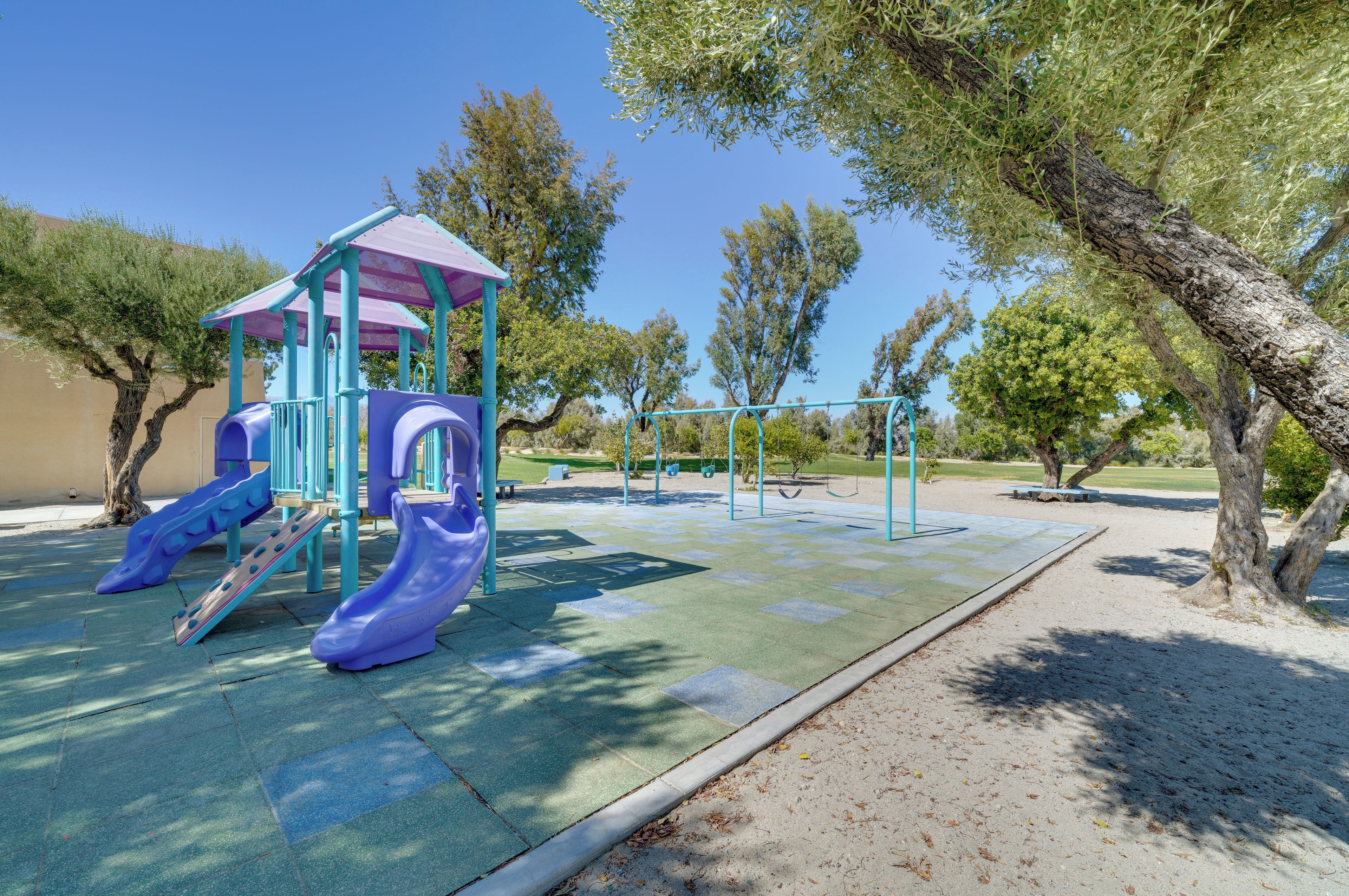 A playground with slides and swings, surrounded by trees and a clear sky.