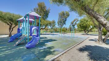 A playground with slides and swings, surrounded by trees and a clear sky.