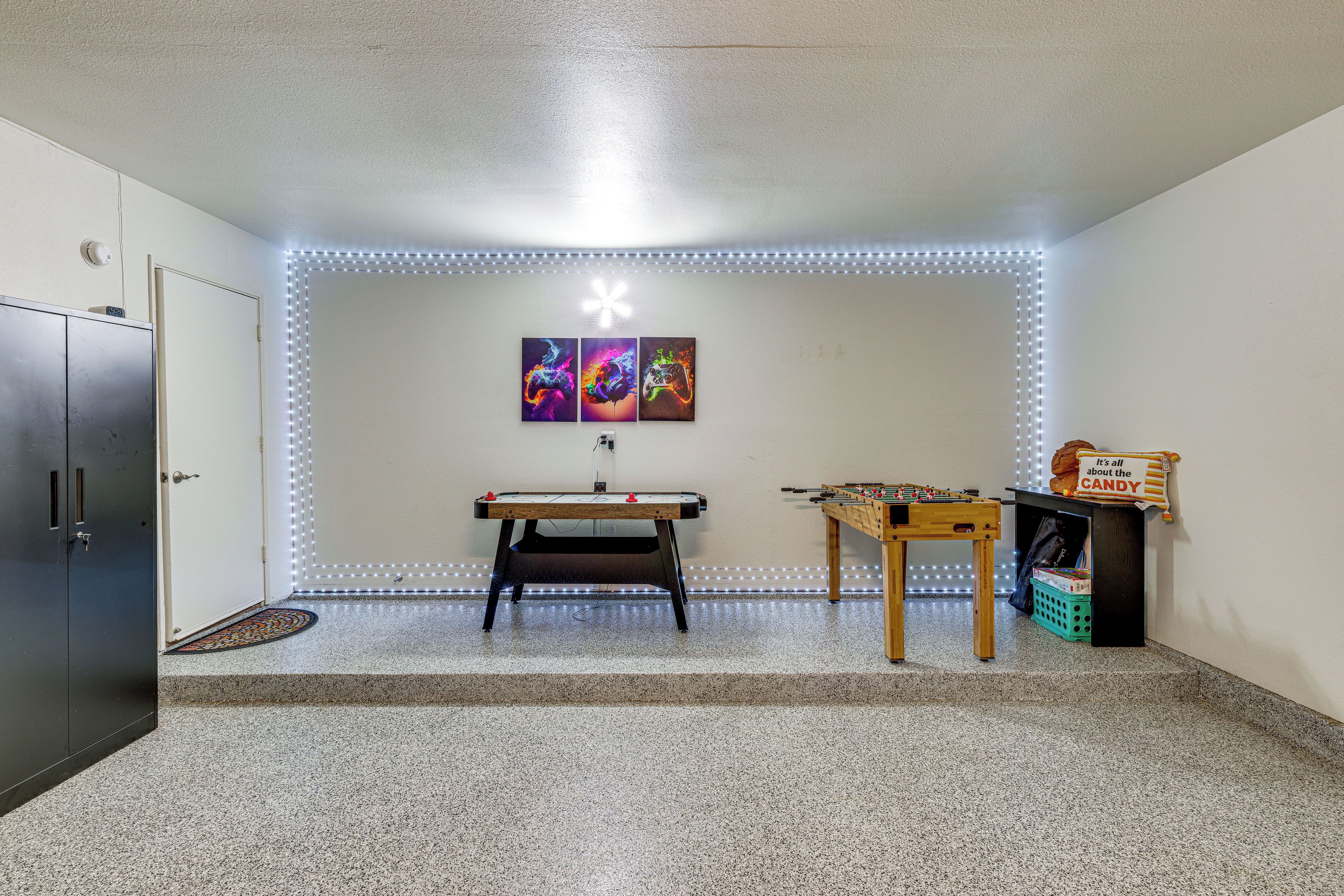 A room with a foosball table, a pool table, and LED strip lighting along the walls.